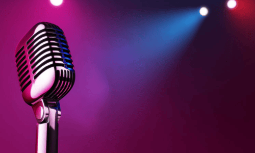 Close-up of a vintage microphone on stage with colorful purple and blue spotlights in the background.