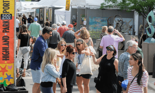 Crowds of people walk through the Port Clinton Art Festival in Highland Park, browsing artist booths and outdoor exhibits on a sunny day.