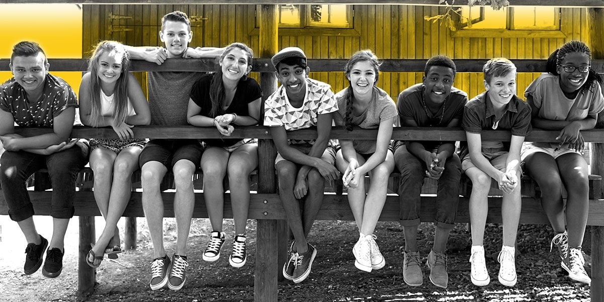 Nine boys and girls hang out along a fence at a summer camp for kids