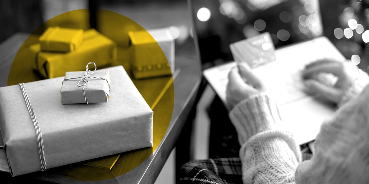 A woman using her credit card to do online holiday shopping, with wrapped packages in the foreground