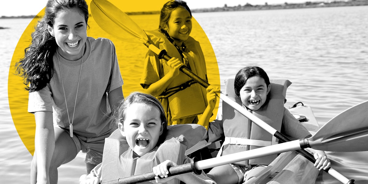 A female camp counselor with three young girl campers learning how to kayak