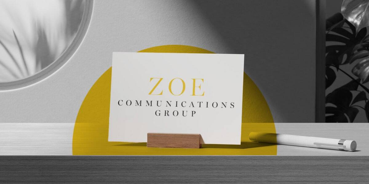 A Zoe Communications Group business card sits on a small wooden stand